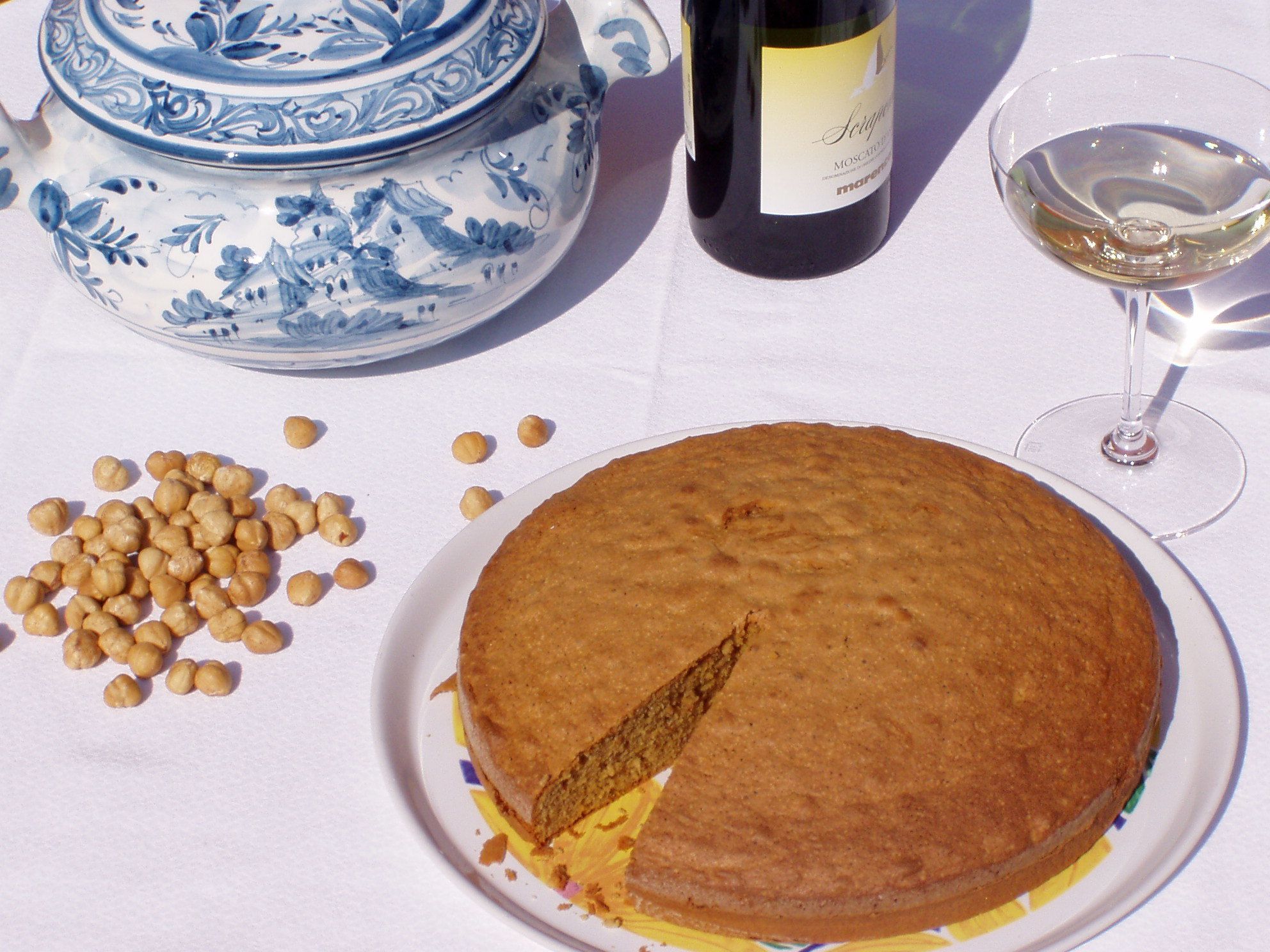 A table with a cake, a bottle of wine, a glass of wine, and a blue and white ceramic set.
