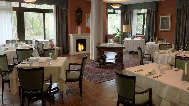 A dining area with multiple tables and chairs, a fireplace, and large windows with curtains.