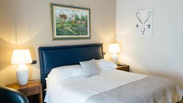 A neatly made bed with white linens, two bedside lamps, a framed landscape painting, and a wall art piece.
