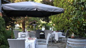 An outdoor dining area with wicker chairs and tables, covered by a large umbrella.