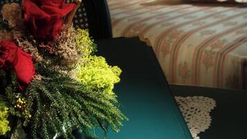 Quarto de hotel com cama bem arrumada, um arranjo floral decorativo e um livro verde intitulado 'HOTEL RESTORANTE SAN CARLO CORTEMILIA' sobre a mesa.