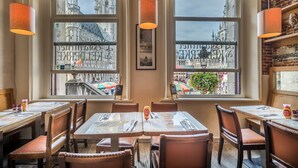 Un restaurante con mesas y sillas de madera, amplios ventanales con vistas a la ciudad y lámparas colgantes.