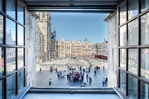 Une vue depuis une fenêtre donnant sur une place historique, avec un grand bâtiment en arrière-plan.