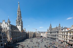 Une place historique, ornée de bâtiments magnifiques, dominée par une tour imposante et animée par une foule nombreuse.