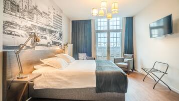 Habitación de hotel moderna con una cama grande, un escritorio, una silla, un televisor y una ventana con cortinas.