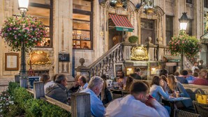 Un café al aire libre con arquitectura de piedra, mesas exteriores y arreglos florales.