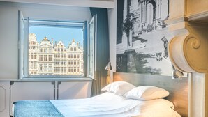Una habitación de hotel con un ventanal grande, una cama, una mesita de noche y una lámpara de pared.