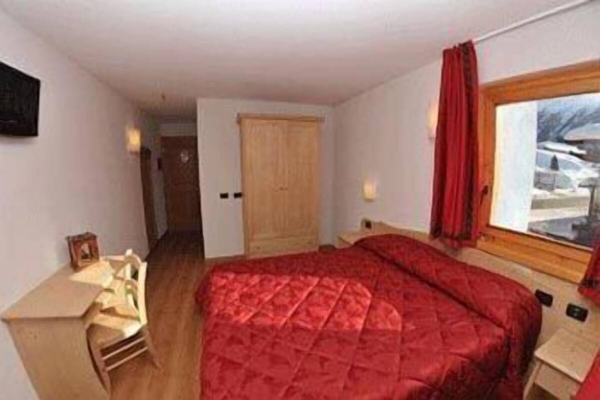 Ein Schlafzimmer mit einem großen Bett, einem Holztisch, einem Stuhl, einem Kleiderschrank und einem Fenster mit Blick auf eine verschneite Landschaft.