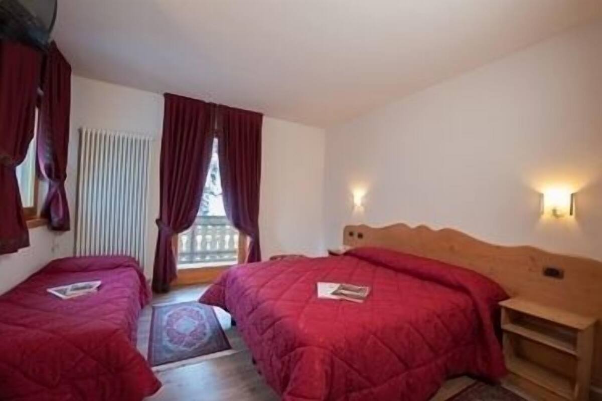 Ein Schlafzimmer mit zwei Einzelbetten, einem Holzkopfstück, einem Fenster mit Vorhängen und einem kleinen Nachttisch.