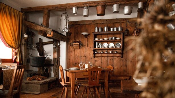 A rustic dining room with wooden furniture, a fireplace, and shelves with kitchenware. - Genzianella (Valfurva)