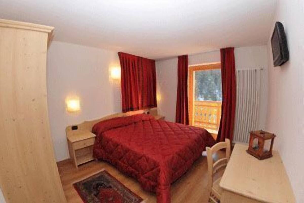 Ein Schlafzimmer mit Bett, Nachttisch, Schreibtisch und einem Fenster mit Vorhängen.