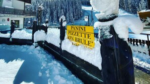 A snowman with a sign in front of a hotel named "BAR Hotel Genziella" with a view of snow-covered trees and mountains in the background. - Genzianella (Valfurva)
