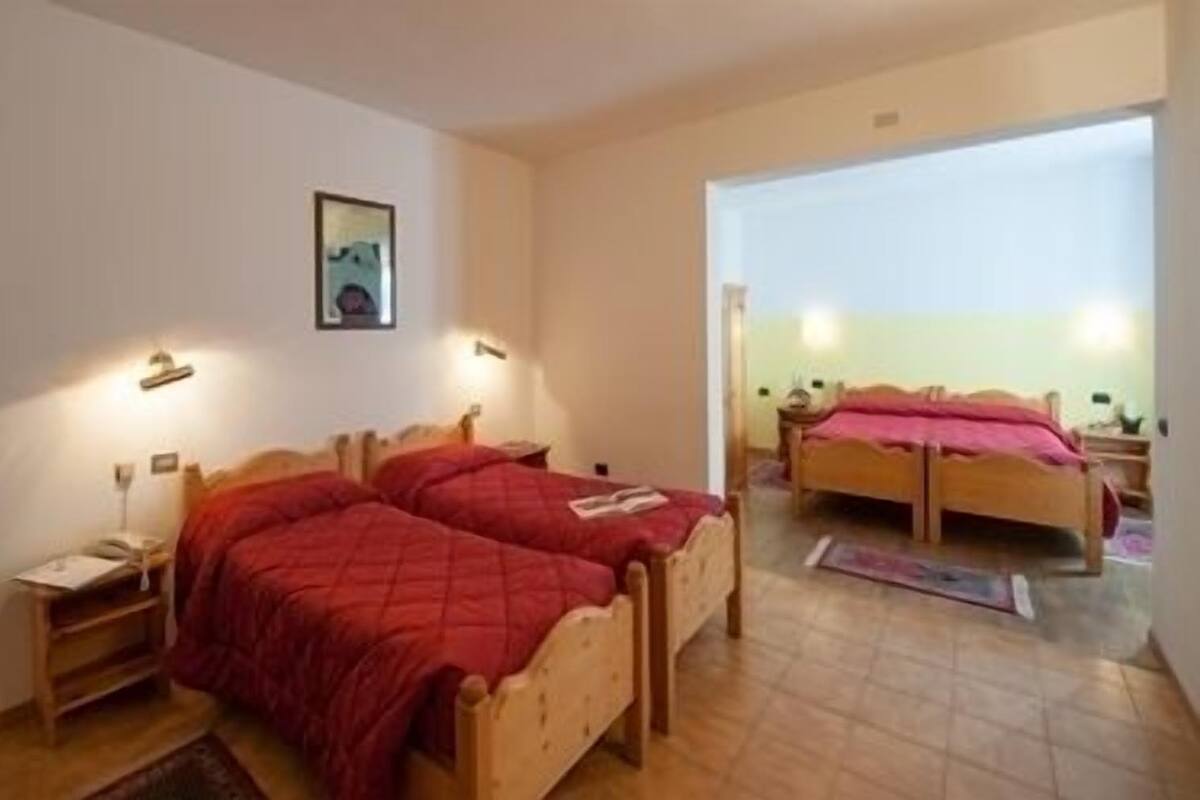 Ein Zimmer mit zwei hölzernen Betten, jeweils mit einer roten Decke, einem Nachttisch mit einer Lampe und einem gerahmten Bild an der Wand.