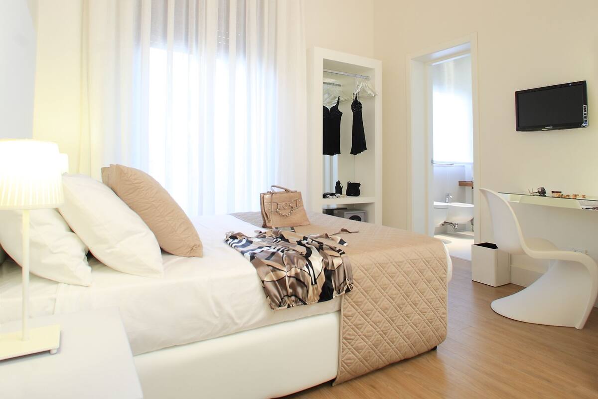 A modern hotel room with a large bed, a sitting area, a mirror, a television, and a ceiling with a circular skylight.