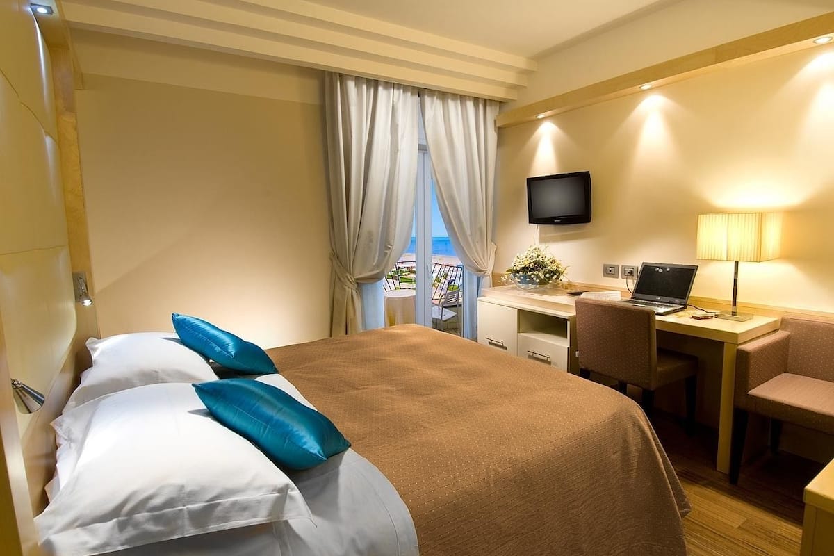 Een hotelkamer met een bed, een bureau, een laptop, een televisie en uitzicht op de omgeving.