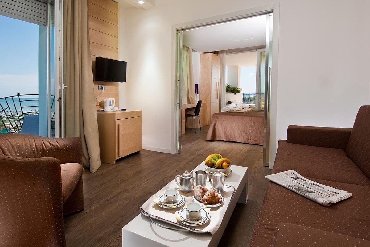 Een moderne hotelkamer met balkon, een zithoek met ontbijtartikelen, een televisie en een gezellige zithoek.