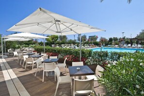 Zona de piscina al aire libre con sillones de descanso y sombrillas, rodeada de follaje y un cielo despejado.