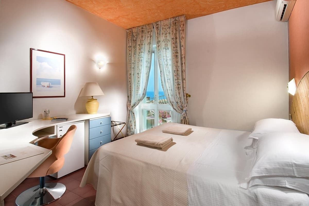 Een hotelkamer met een bed, een bureau, een stoel, een televisie en een raam met gordijnen.