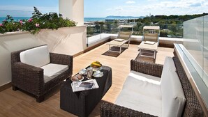 A balcony with wicker furniture, a table with breakfast items, and a view of the sea and distant hills. - Hotel Sarti (Riccione)