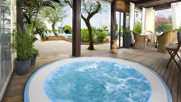 A hot tub area with a wooden deck, potted plants, and wicker furniture. - Hotel Sarti (Riccione)