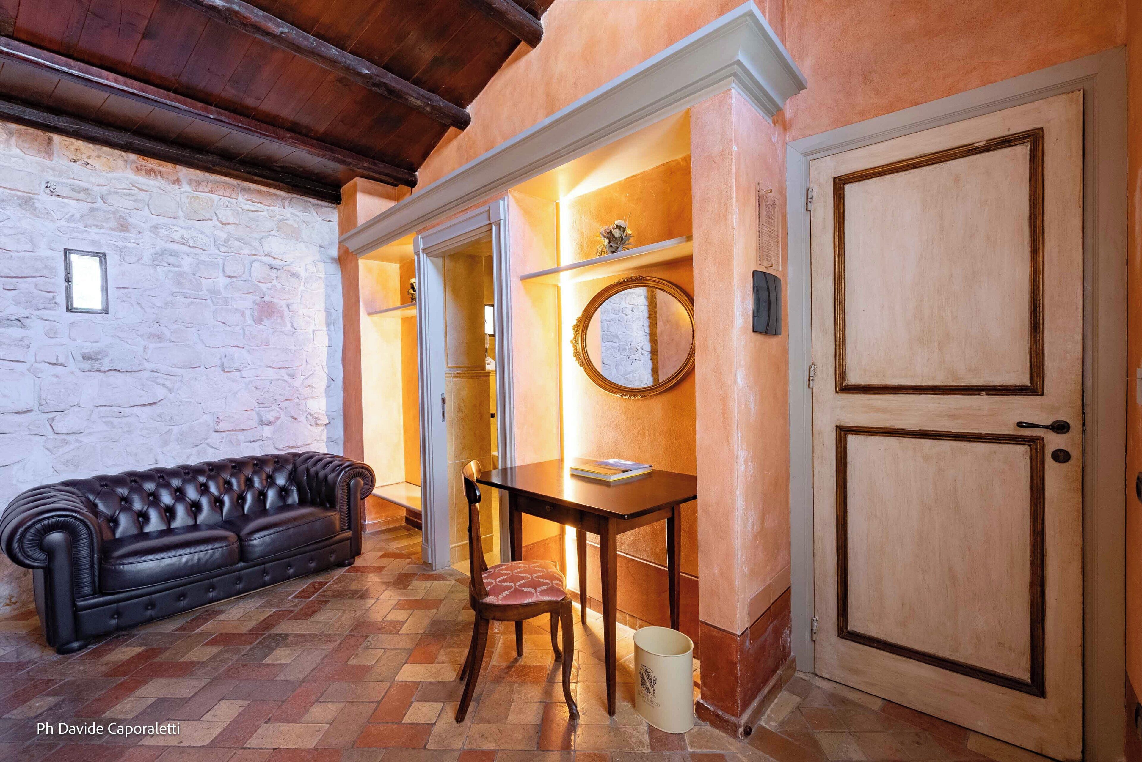 Ein gemütlicher Raum mit Ledersofa, Holztisch und Stuhl. Eine Holztür und eine Steinwand sind sichtbar.