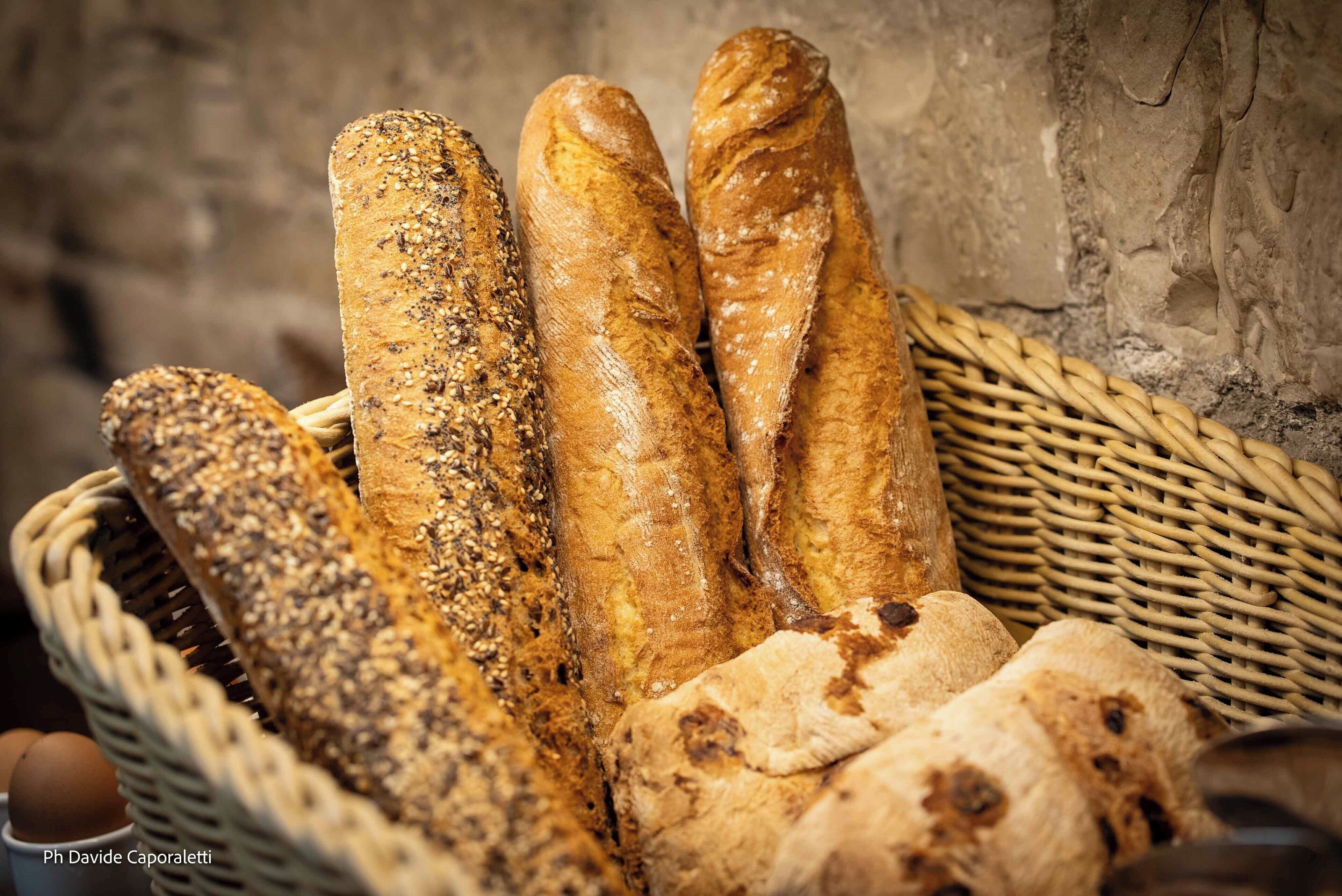 Un panier contenant diverses sortes de pain, notamment un pain aux graines et une baguette, posé sur un autre panier en osier.