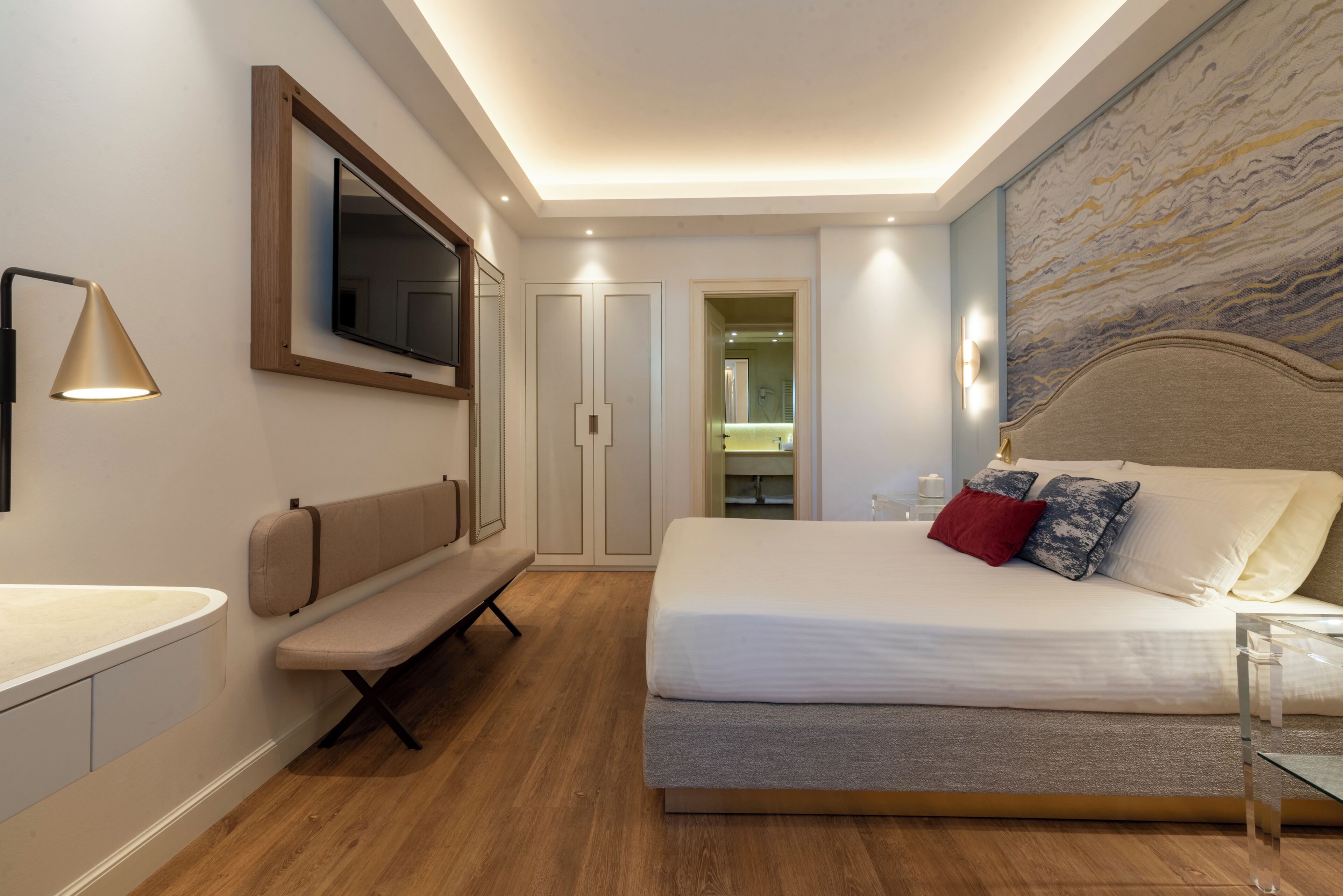 A modern bedroom with a bed, bench, TV, and artwork on the wall.