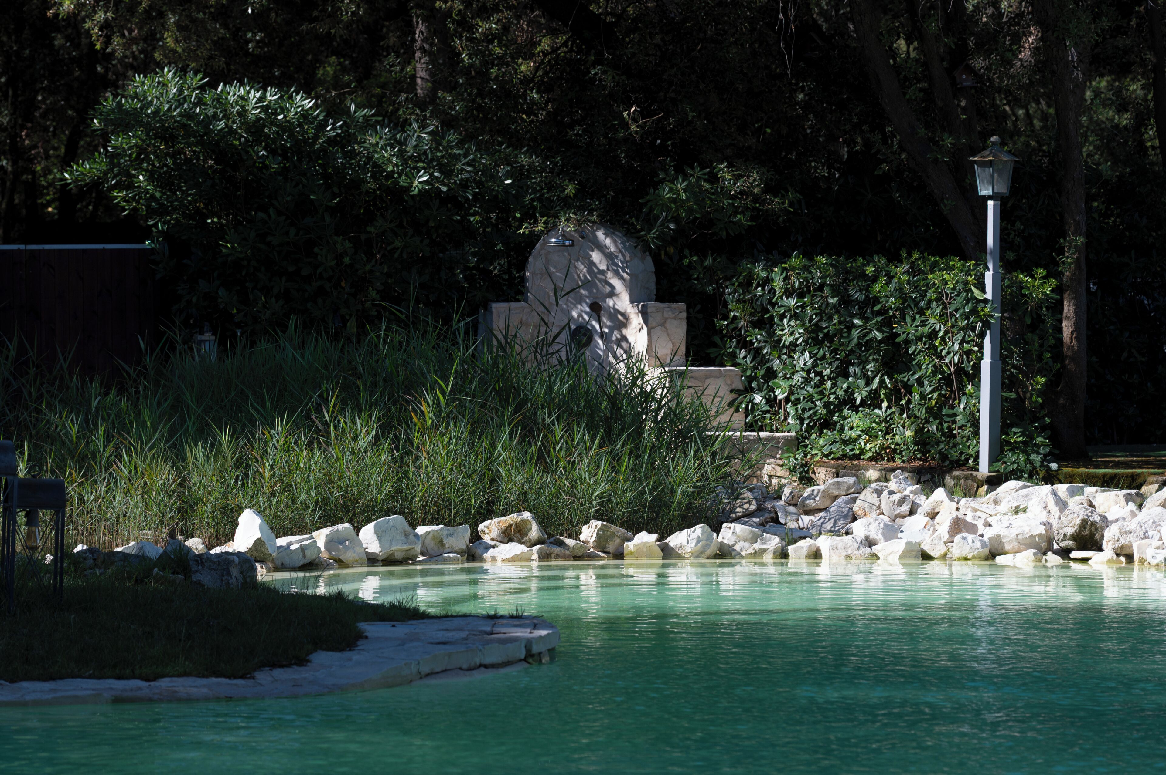 A tranquil outdoor pool area with clear water, surrounded by rocks and greenery.