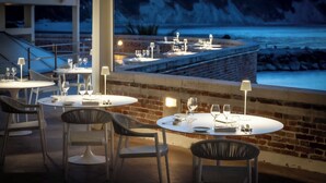 Een terras met tafels en stoelen, een bakstenen muur en uitzicht op het water.