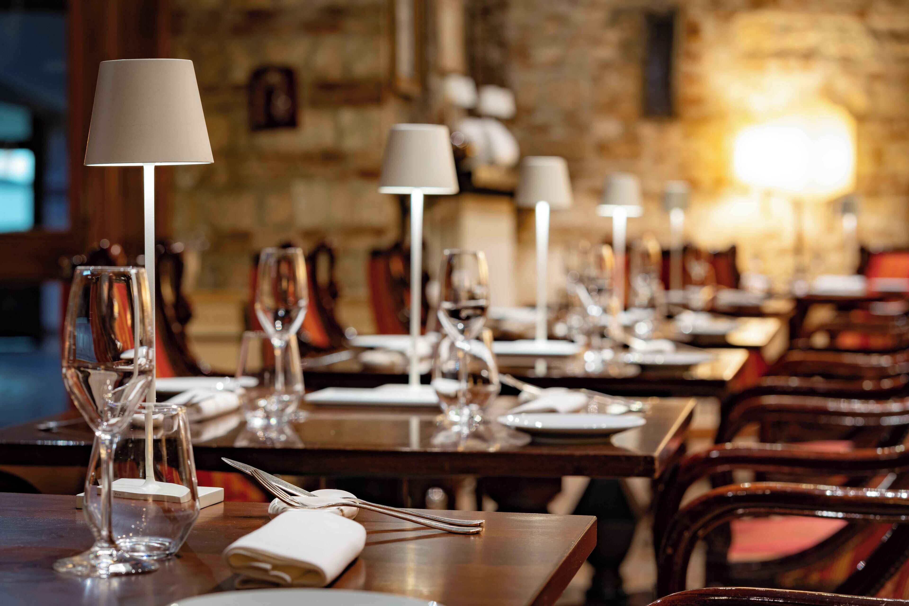 A restaurant with tables set for dining, each with a wine glass, a plate, and cutlery.