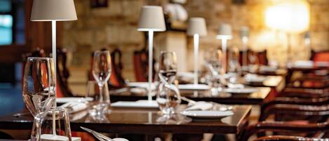 Un restaurante con mesas dispuestas para comer, cada una con una copa de vino, un plato y cubiertos.