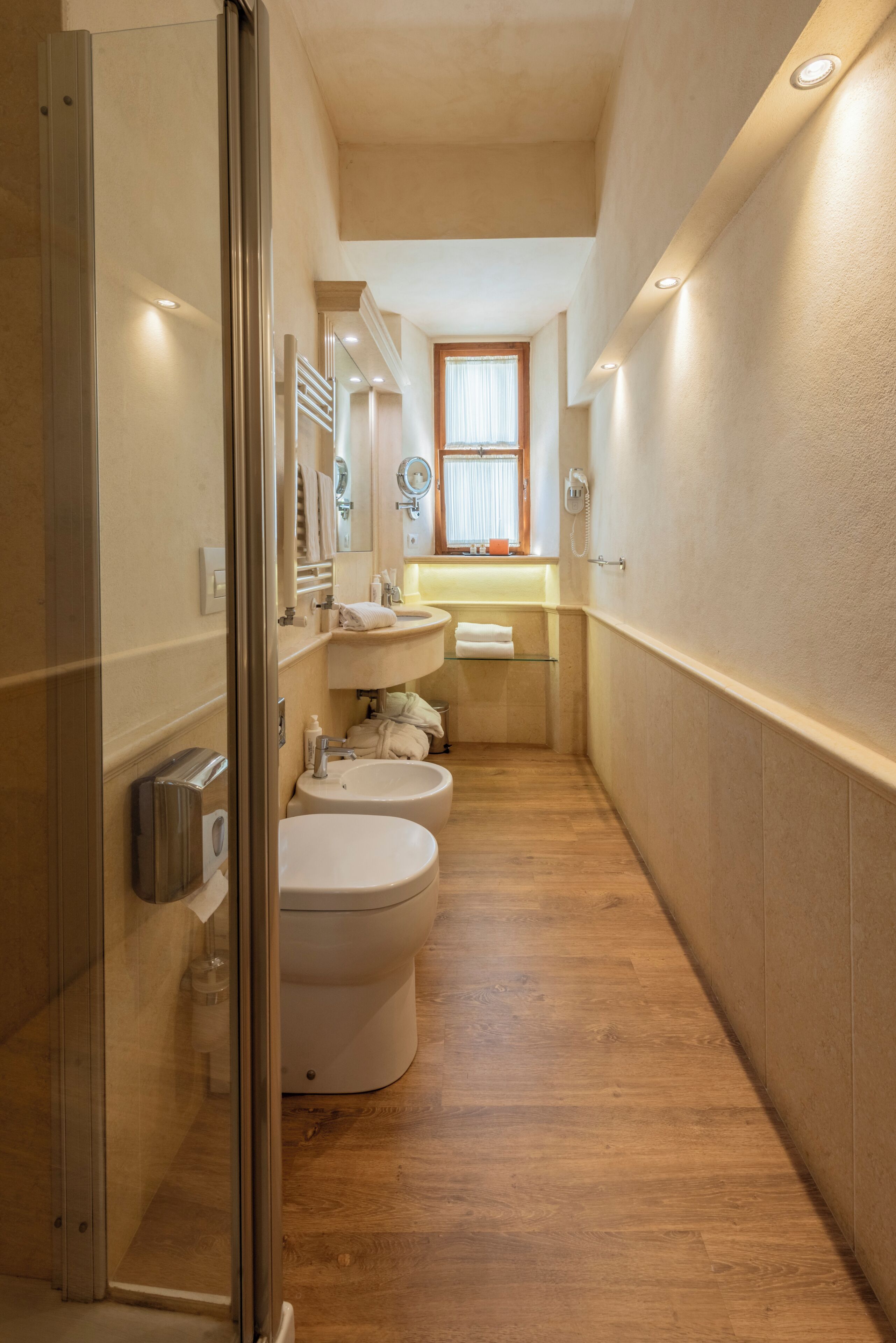 Un baño estrecho con tres inodoros, un lavabo y un espejo.