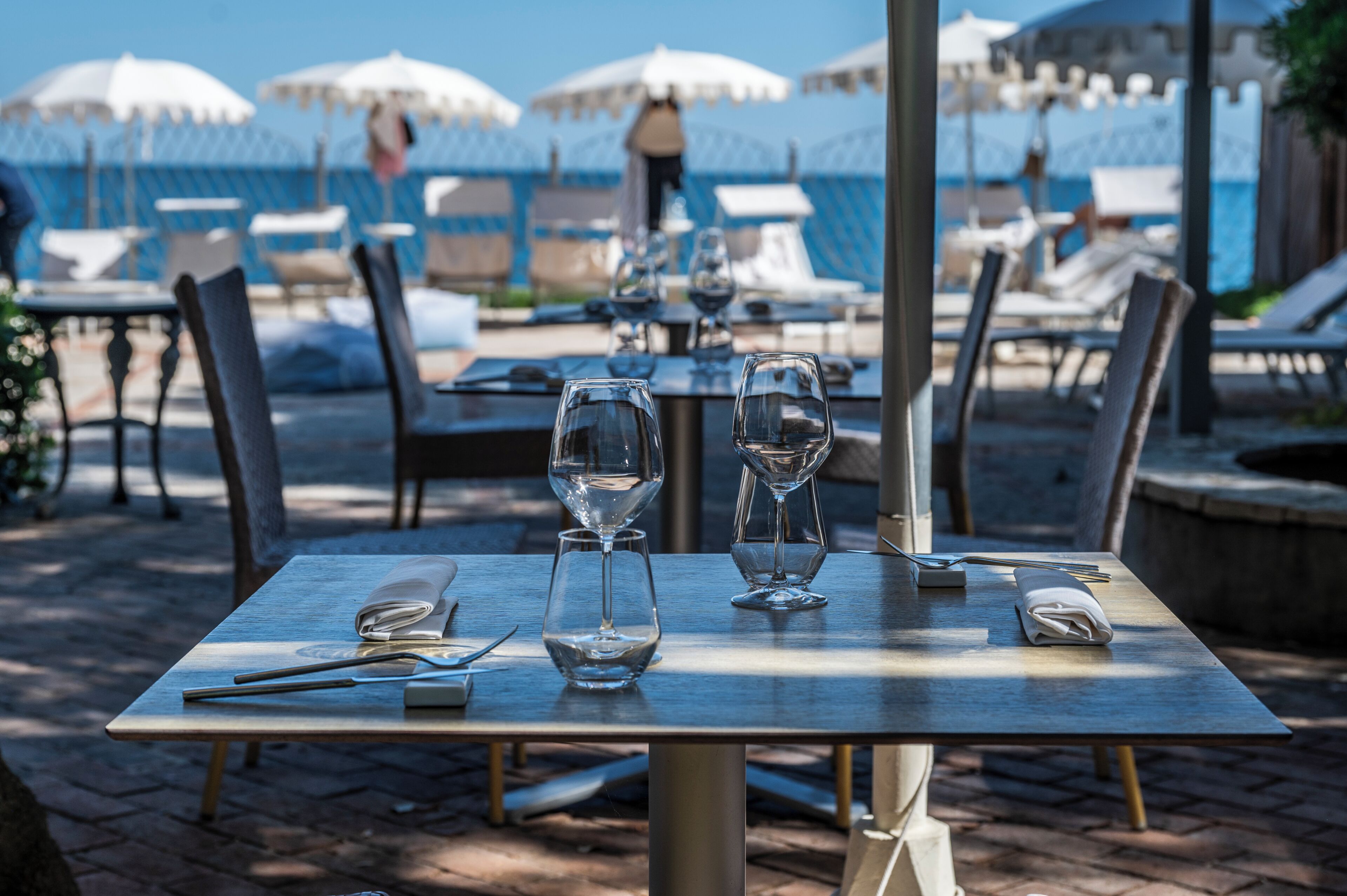 An outdoor dining area with tables set for two, each with cutlery and a glass.