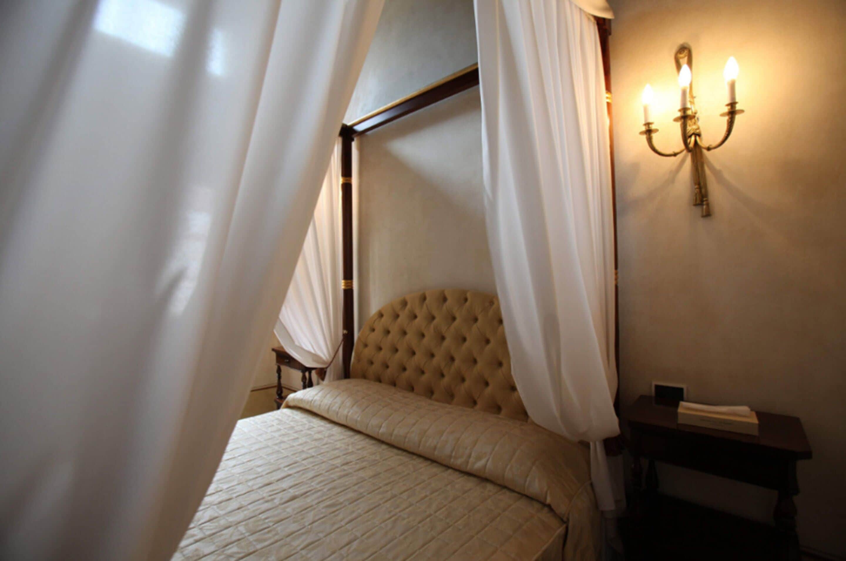 Une chambre à coucher avec un lit à baldaquin, une table de chevet et un luminaire fixé au mur.