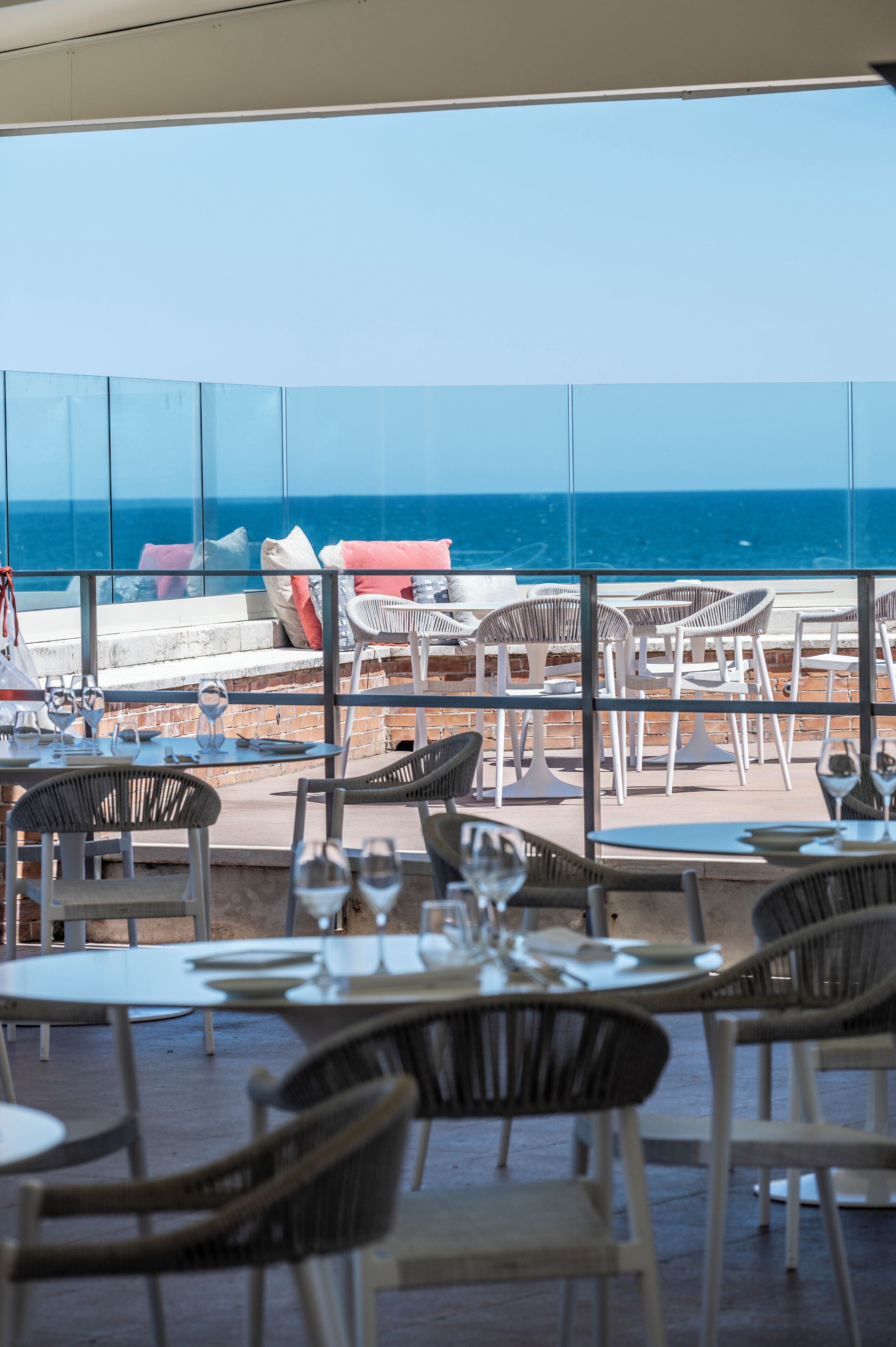 A restaurant with outdoor seating overlooking the sea, featuring tables and chairs.