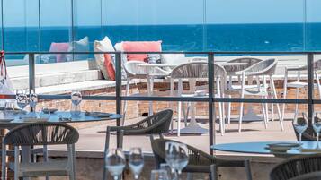 A restaurant with outdoor seating overlooking the sea, featuring tables and chairs.