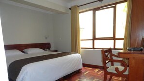 Ein Hotelzimmer mit einem Bett, einem Schreibtisch mit einem Laptop und einem Fenster mit Vorhängen.