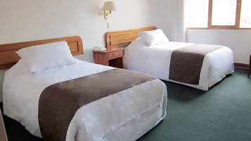Dos camas individuales con cabeceros de madera, una mesita de noche con lámpara y una ventana con cortinas.
