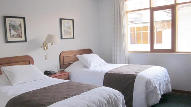 A hotel room with two beds, a nightstand, a lamp, and two framed pictures on the wall. - Emperador Plaza (Cusco)