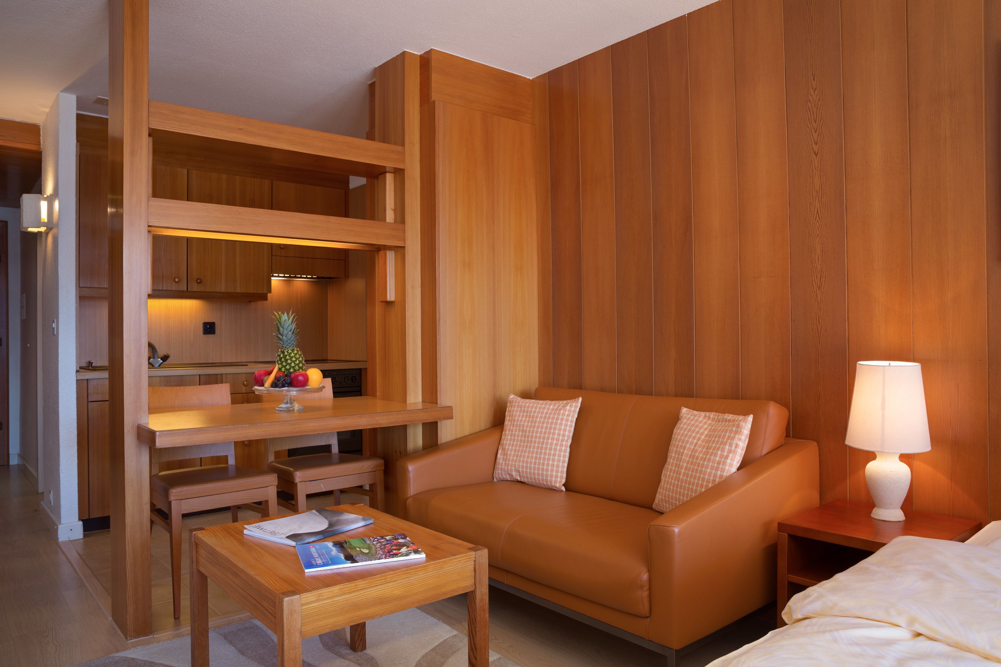 Une chambre d’hôtel compacte comprenant un coin cuisine, un canapé, une petite table et une lampe de chevet.