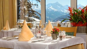 Mesa dispuesta para comer con vista a la montaña, un jarrón de flores rojas y un juego de salero y pimentero.