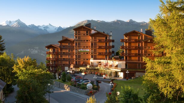 Un hotel de varios pisos con fachada de madera, balcones y vista a montañas nevadas.
