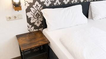 Une chambre d’hôtel bien aménagée, avec un lit, une table de chevet, une lampe fixée au mur et des prises électriques.