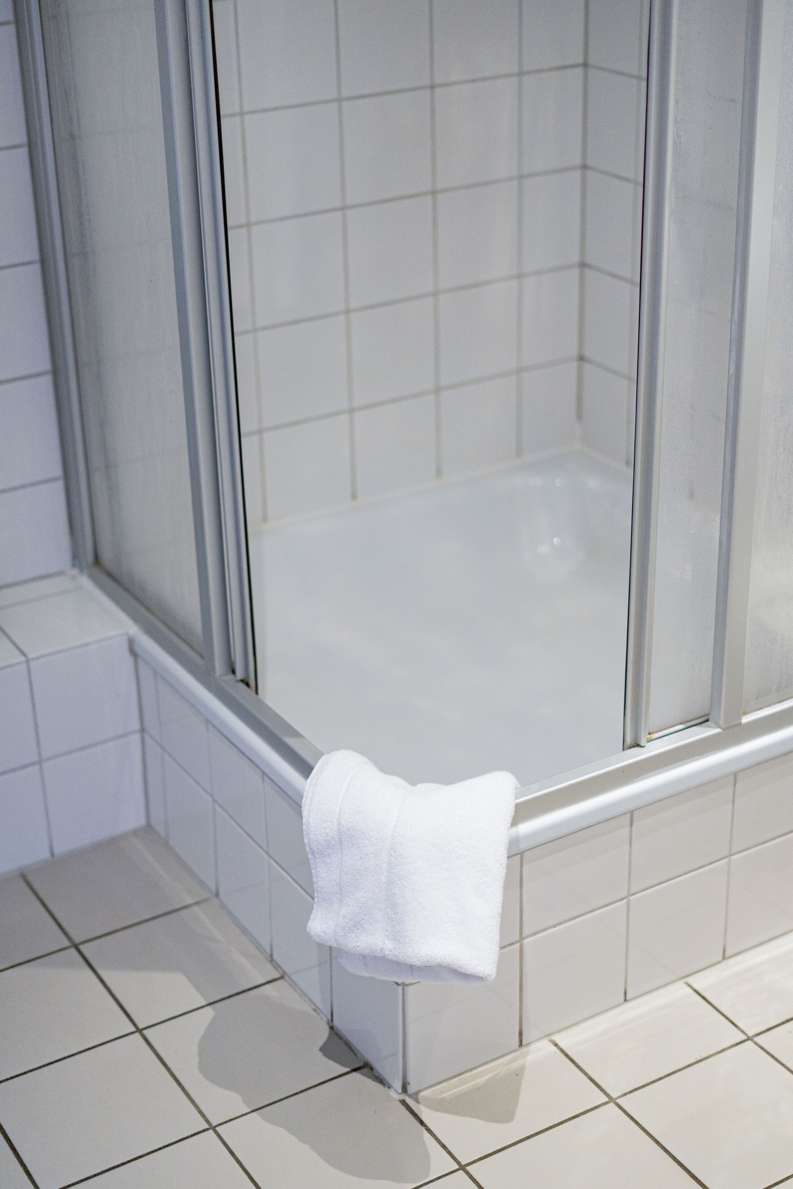 A bathroom with a glass shower enclosure, white tiled walls, and a white towel hanging on the shower door.