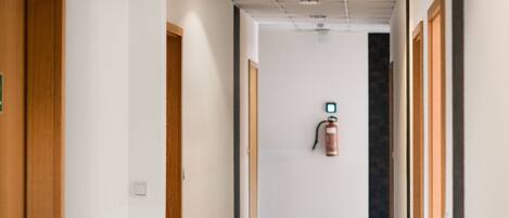 A corridor with wooden doors, a fire extinguisher mounted on the wall, and a ceiling with recessed lighting.