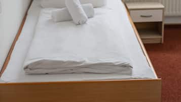 A neatly made bed with white linens and pillows, a bedside table with a lamp, and a window with a view of buildings outside.