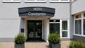 En hotellentréd med en skylt som visar texten ”HOTEL Constantin”, stora fönster och krukväxter.