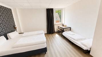 Une chambre d’hôtel avec deux lits, un bureau et une fenêtre avec des rideaux.