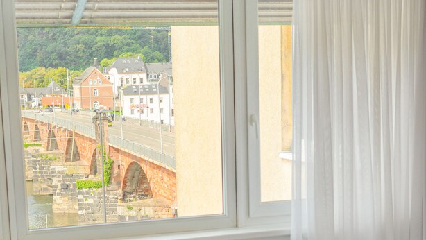 Habitación de hotel con un ventanal grande, una cama y vistas a un puente y edificios.