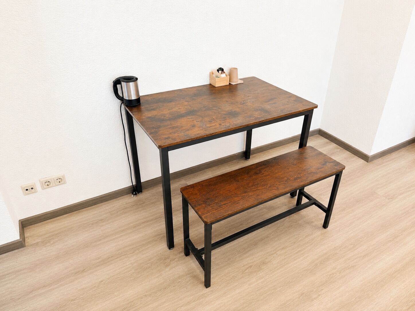 A small wooden table with a bench, a kettle, and a box of tissues.